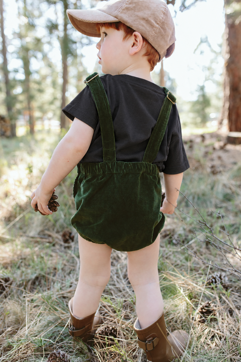 OVERSIZED TEE in asphalt black worn under green corduroy overalls by a toddler in the forest