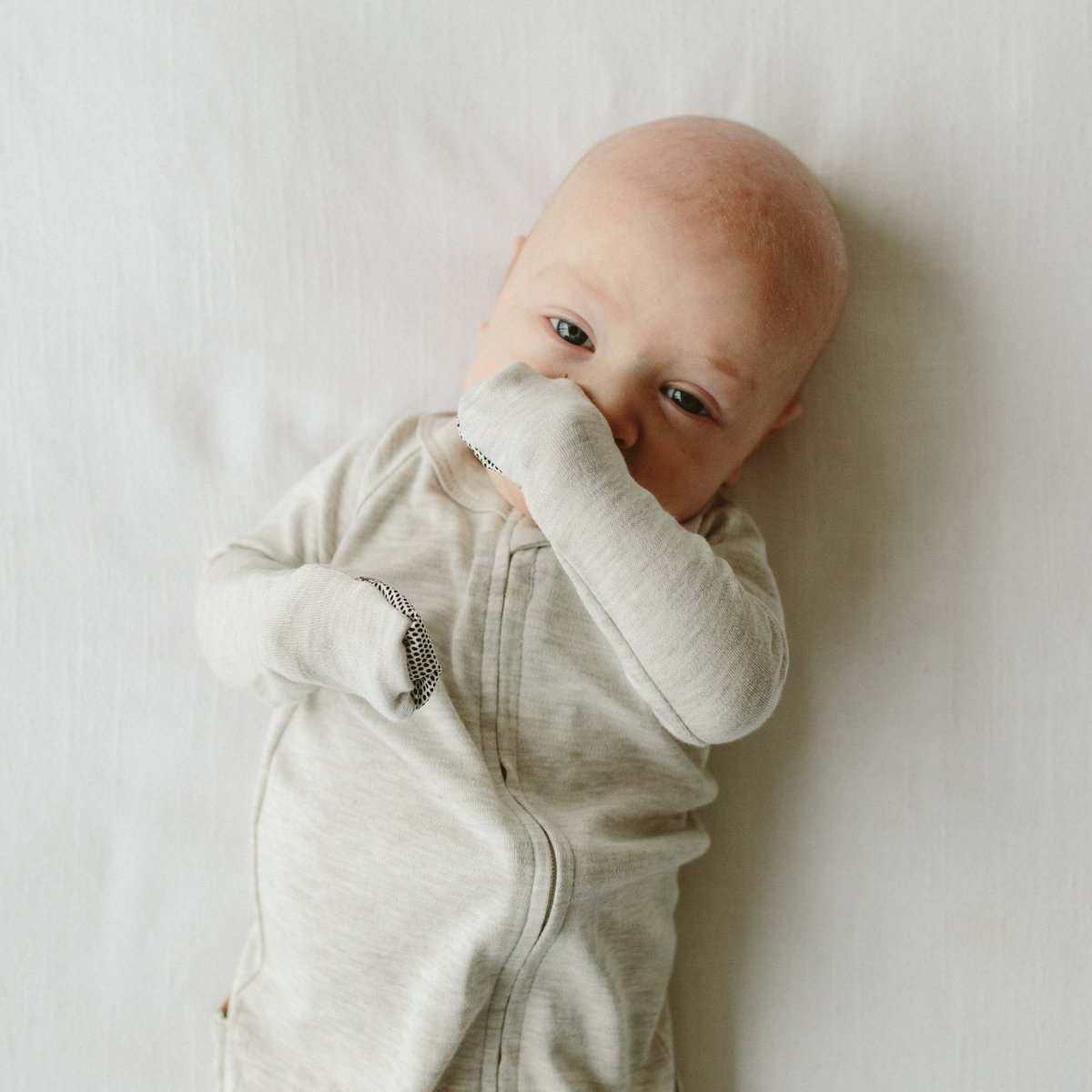 GROW WITH YOU FOOTIE, a light gray long-sleeve baby footie in soft solid fabric with a two-way front zipper and built-in mitts.