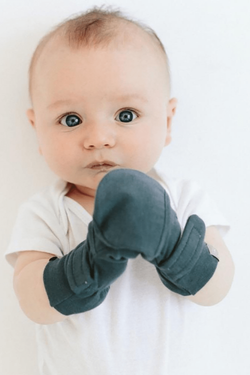 PREEMIE STAY ON MITTS in solid dark gray soft fabric, with adjustable wraparound closures covering a baby's hands