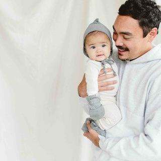 STAY ON 2-PACK MITTS in soft grey fabric with a ribbed wrist cuff, worn by a baby in a parent’s arms