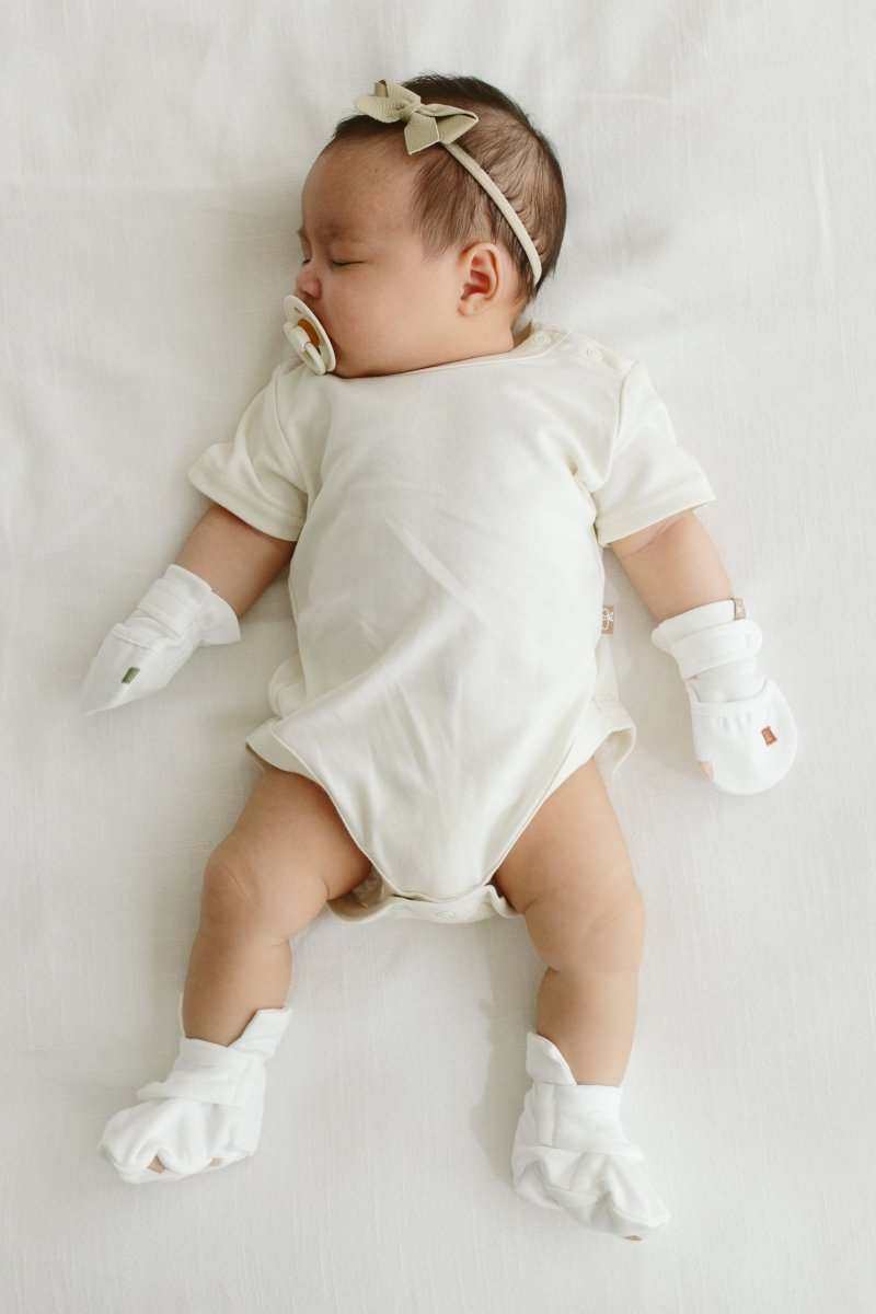 STAY ON 2-PACK MITTS in white soft fabric with adjustable stay-on closures, worn by a baby