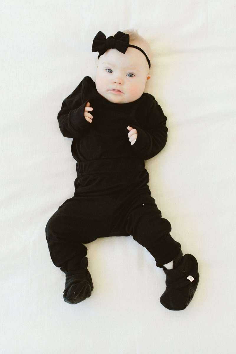 Stay On Boots are black baby booties with a soft fabric finish and adjustable wrap closures, worn with a matching outfit