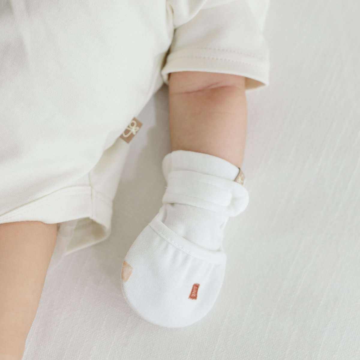 Stay on mitts in soft white fabric with adjustable wraparound closures and a small rust-colored tag