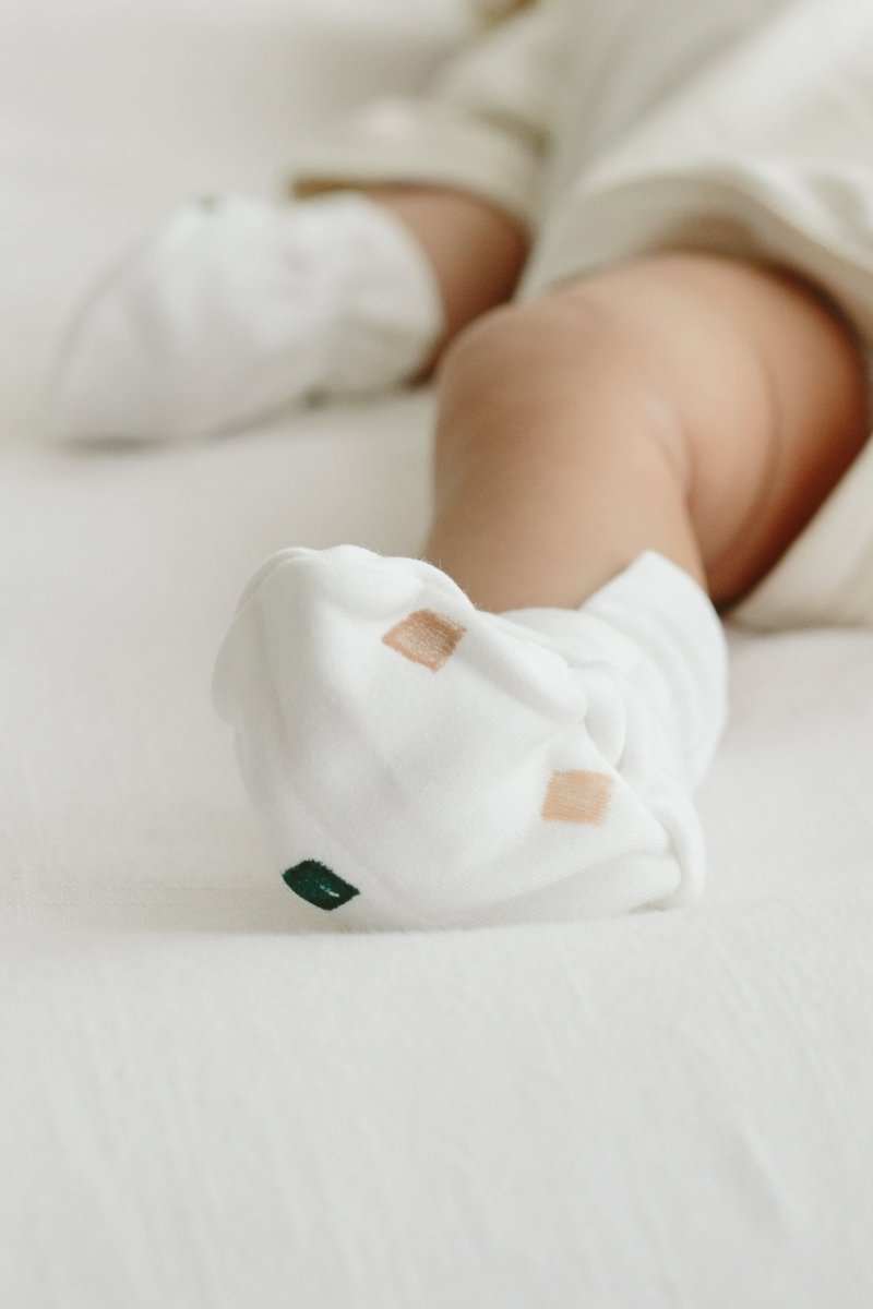 Baby stay on mitts and booties in soft white fabric with small tan and green geometric accents and adjustable cuffs