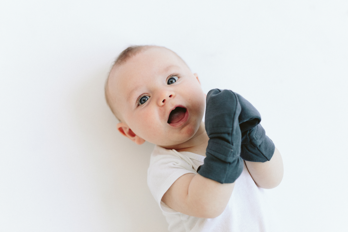 Welcome Home Set with a baby wearing charcoal blue mitts and a white short-sleeve outfit, featuring soft fabric and gathered cuffs