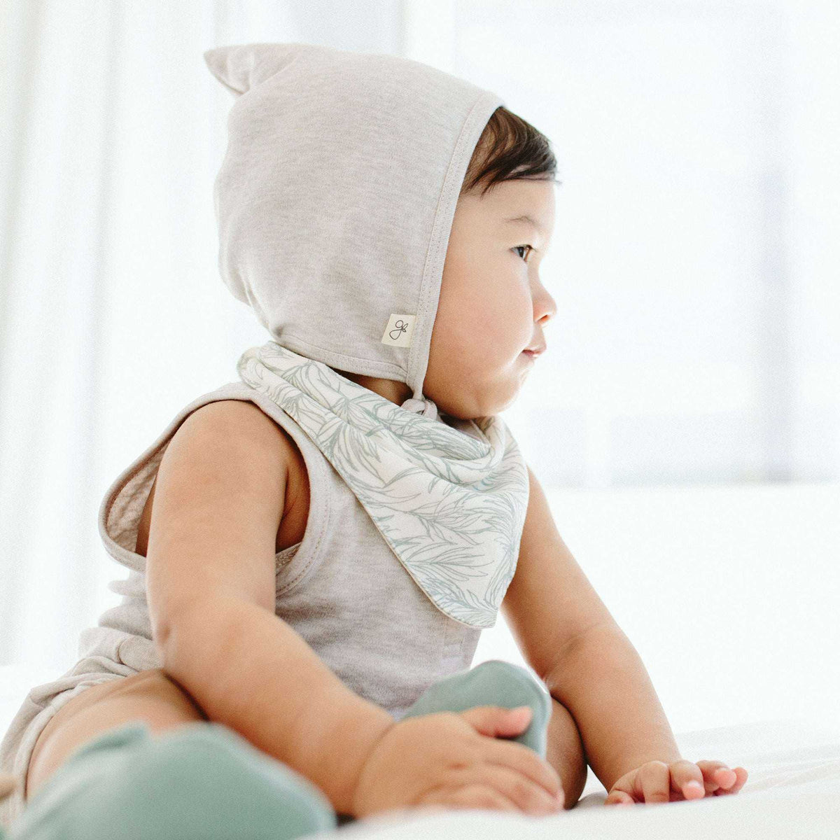 Welcome Home Set shows a baby in a light gray sleeveless outfit and hood with a pale botanical print bib