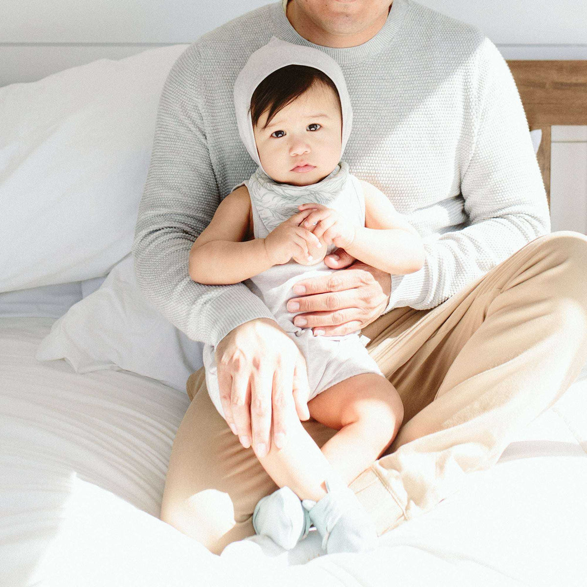BANDIT BONNET in pale gray knit with a rounded pixie-style hood, worn by a baby with a matching light gray outfit