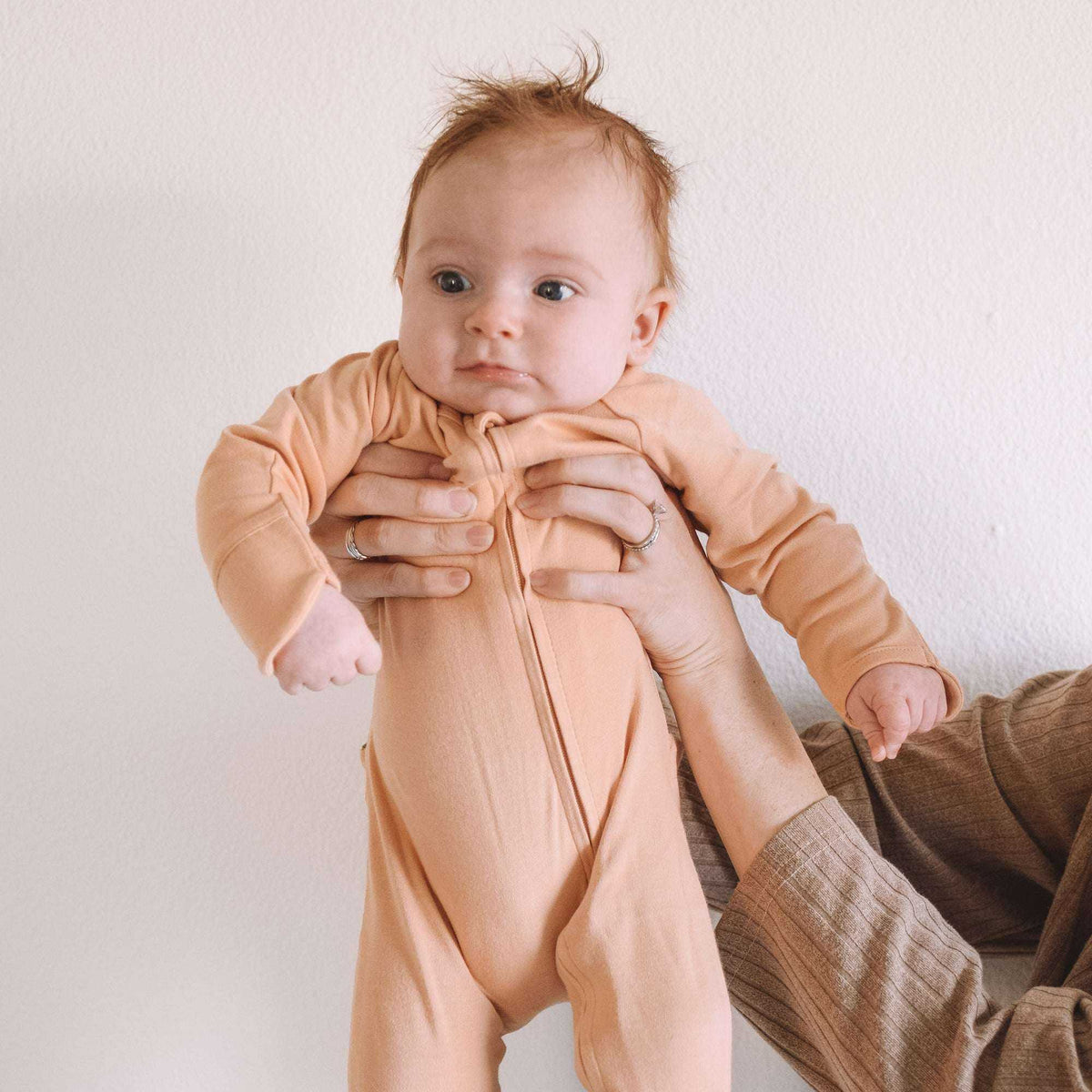 GROW WITH YOU FOOTIE in a peach-toned, soft knit fabric with long sleeves, a front zip and covered feet