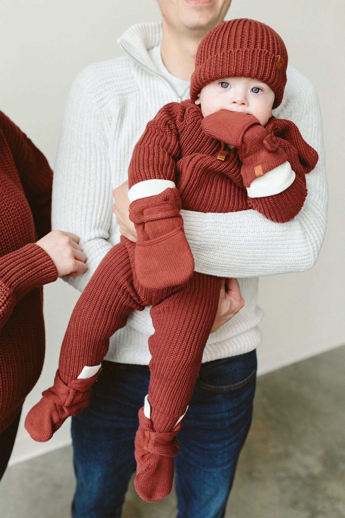 KNIT MITTS in rust-red ribbed knit with fold-over cuffs and soft fleece palms, shown on a baby