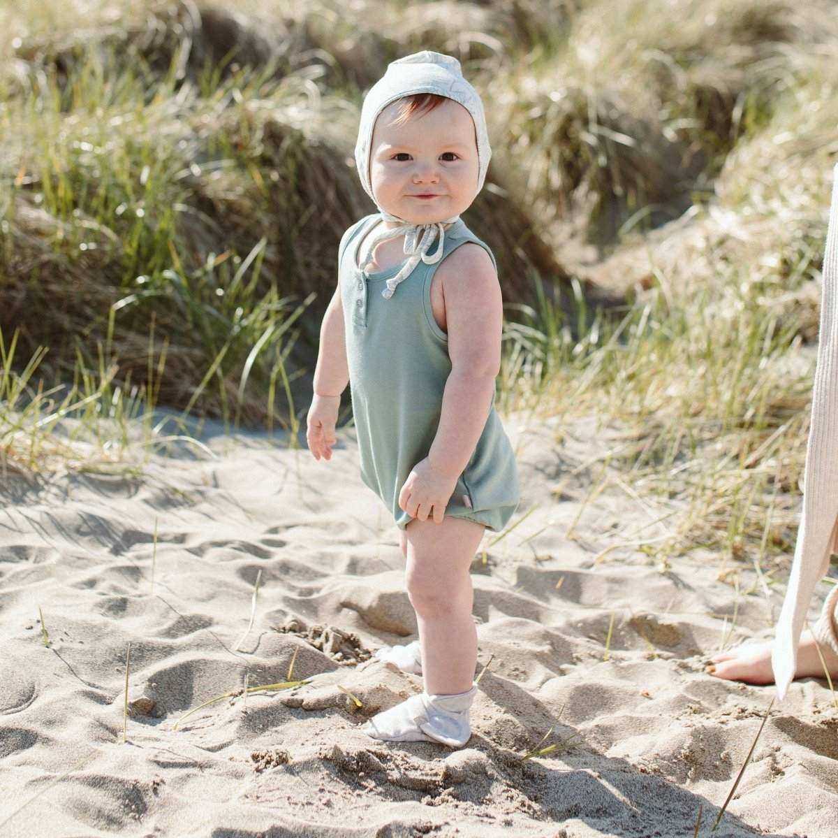 PREEMIE STAY ON BOOTS are pale gray soft baby boots with a simple rounded shape, worn with a muted sage romper.