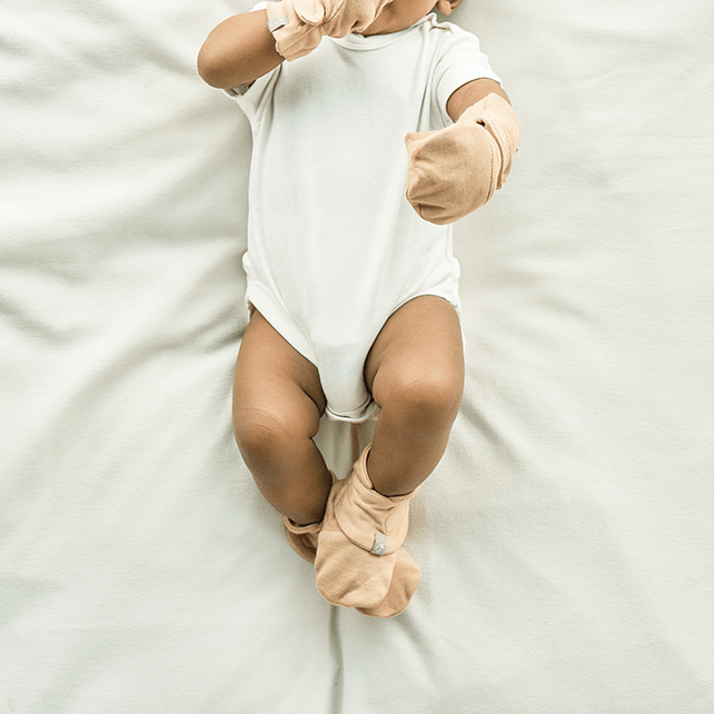 Stay on Boots in sandstone beige, soft fabric with adjustable wrap closures shown on a baby wearing a white bodysuit